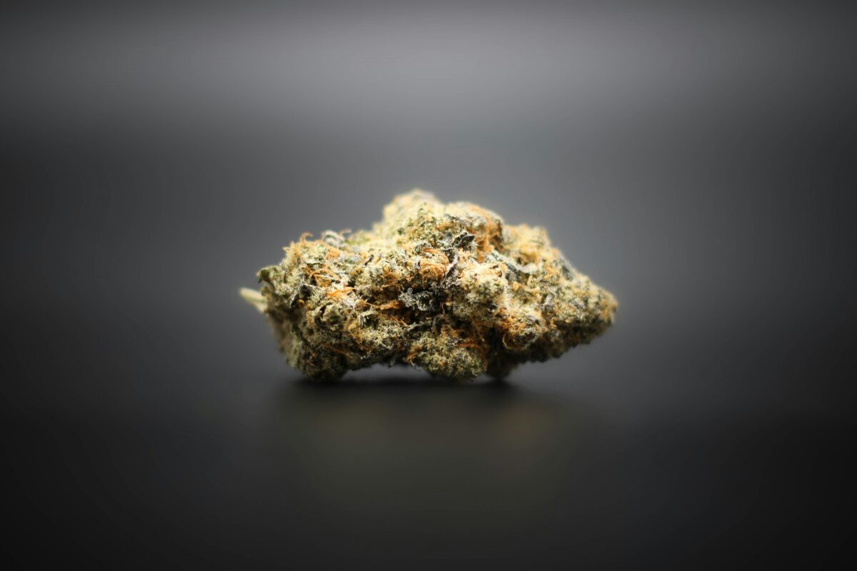 Close-up of a single cannabis bud with frosty trichomes and orange hairs, displayed against a smooth, black background, highlighting its texture and color.