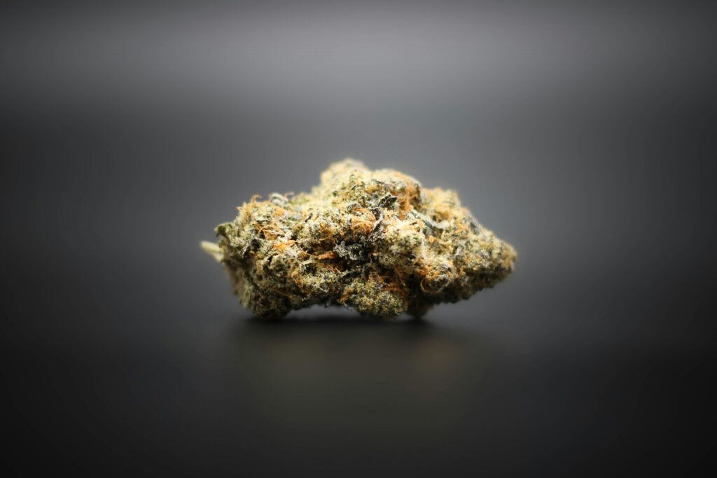 Close-up of a single cannabis bud with frosty trichomes and orange hairs, displayed against a smooth, black background, highlighting its texture and color.