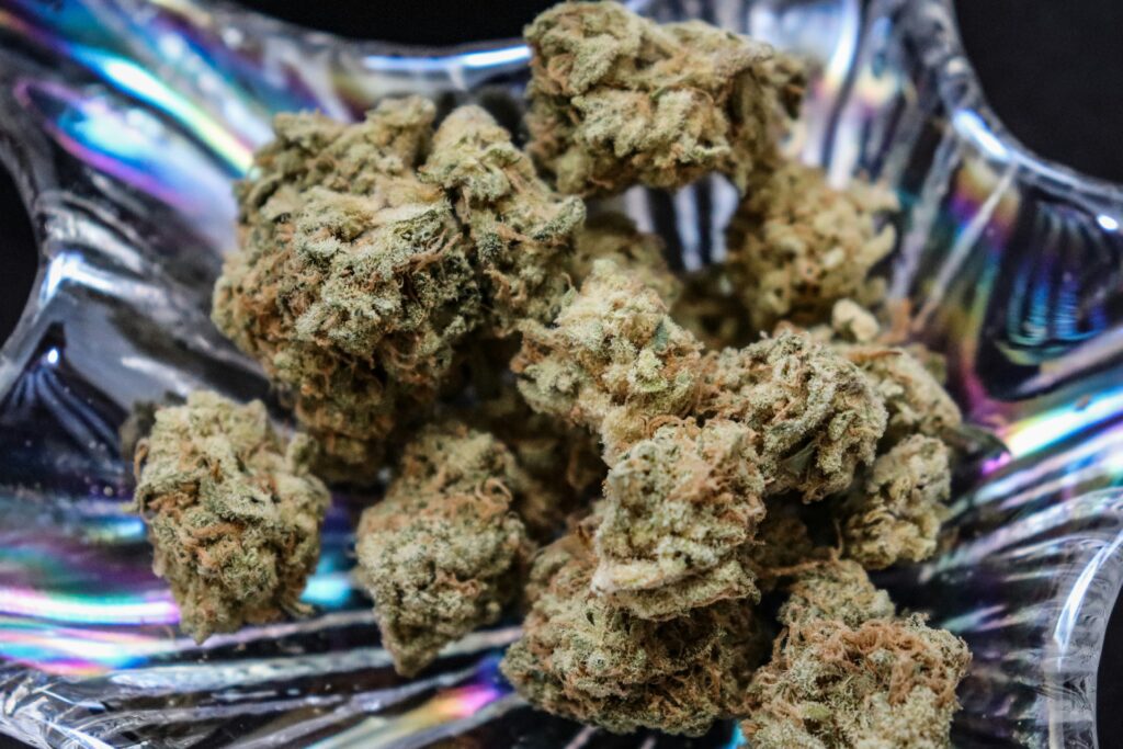 Close-up of cannabis buds in a reflective glass dish, showcasing dense, trichome-covered nugs with hints of orange pistils.