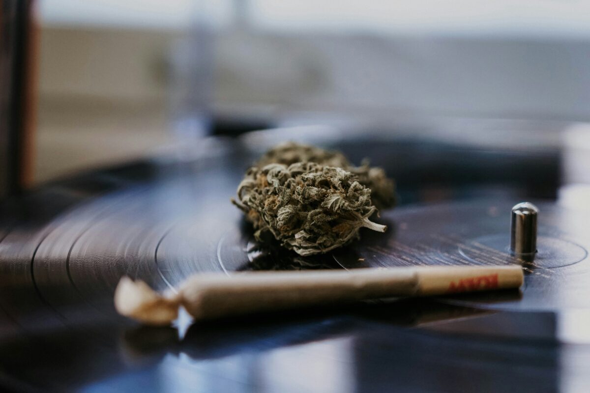 A close-up shot of a cannabis bud and a pre-rolled joint resting on a spinning vinyl record, blending music and cannabis culture in a laid-back, artistic setting.