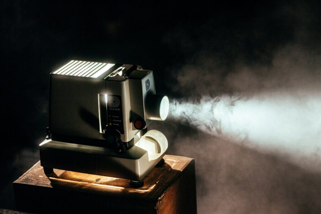 A vintage Dukane projector beams a bright light through a dark, smoky room, creating a nostalgic and cinematic atmosphere, perfect for capturing the essence of retro film experiences.