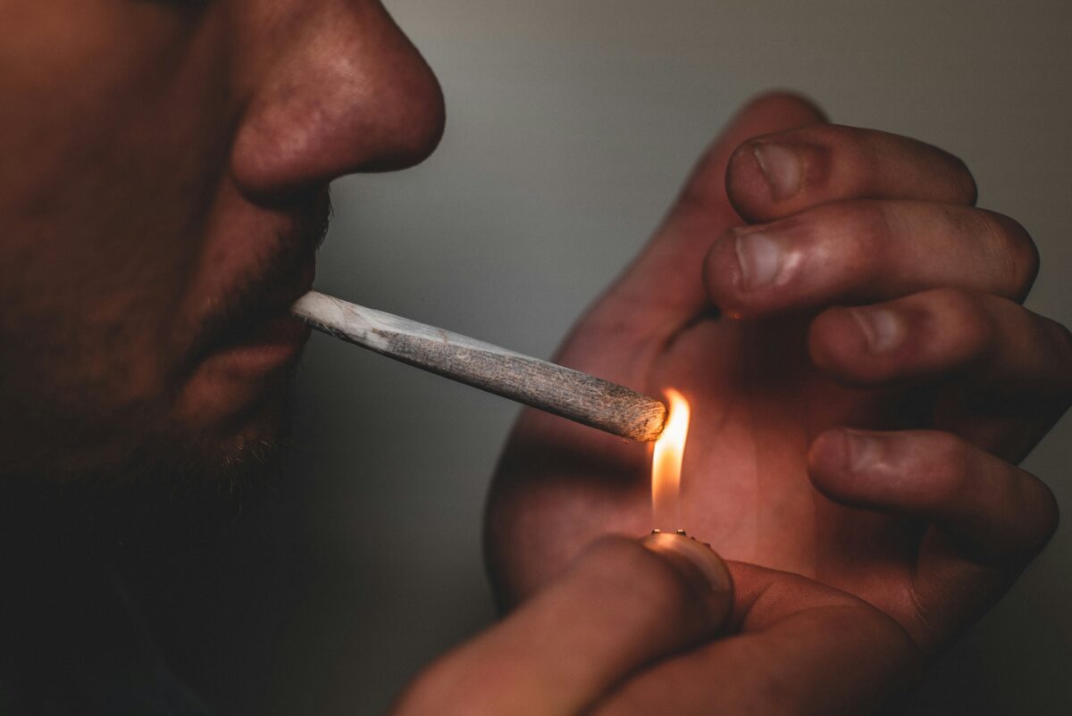 Close-up of a person lighting a cannabis pre-roll with a flame, capturing the moment of inhalation and the warm glow of the lighter.