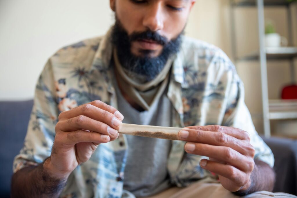 pexels-kampus-7928082 - Nature Med Dispensaries Man in a tropical shirt carefully rolling a cannabis pre-roll, focused on the process in a relaxed indoor setting.