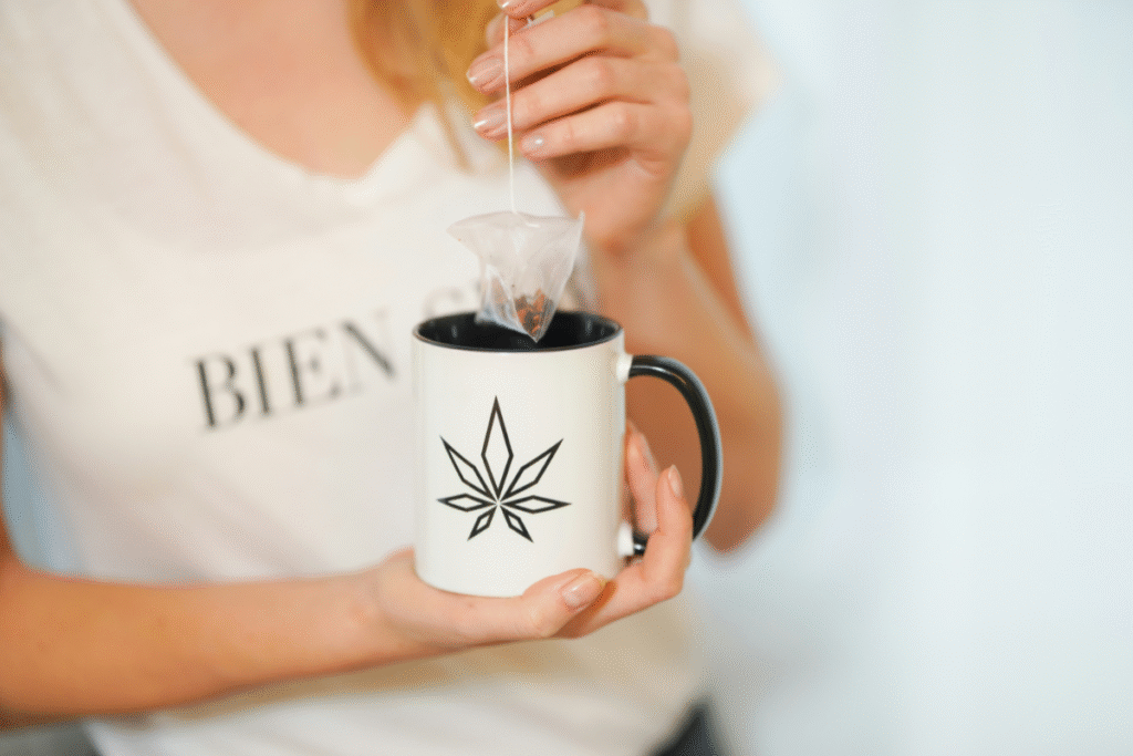 image of a female in a white shirt holding a white and black mug with a cannabis leaf on it dipping a tea bag into the mug