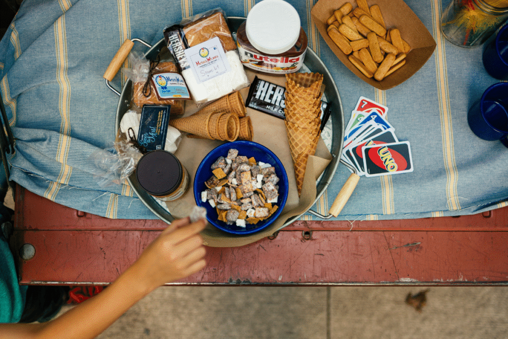 image of a table with a blue striped table cloth with various snacks sitting on the table and a plate. a deck of uno cards sits next to the plate of snacks. there is a hand reaching for some of the snacks.