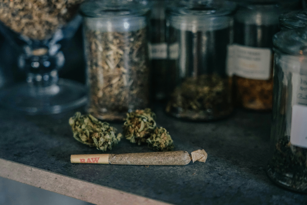 image of a rolled joint sitting on a counter in front of two cannabis mugs in front of jars filled with other herbs