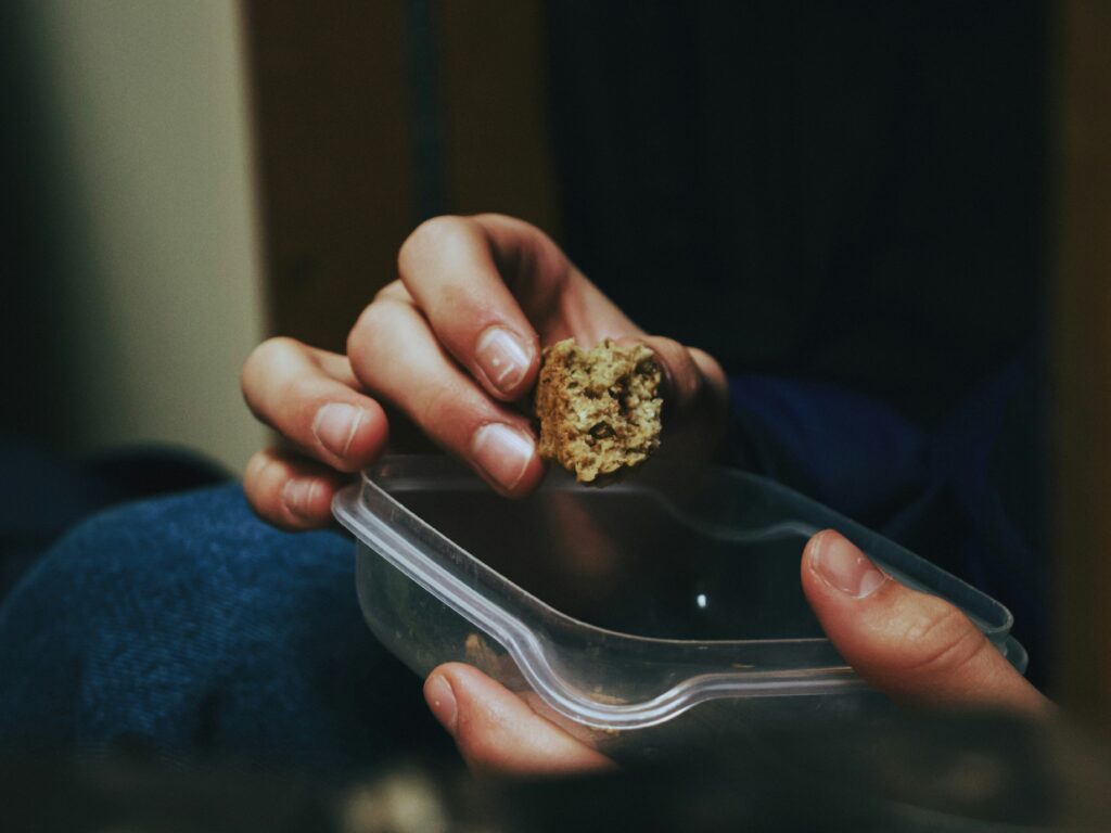 Close-up shot of a person's hands delicately holding a cannabis nug over a clear plastic takeout container.