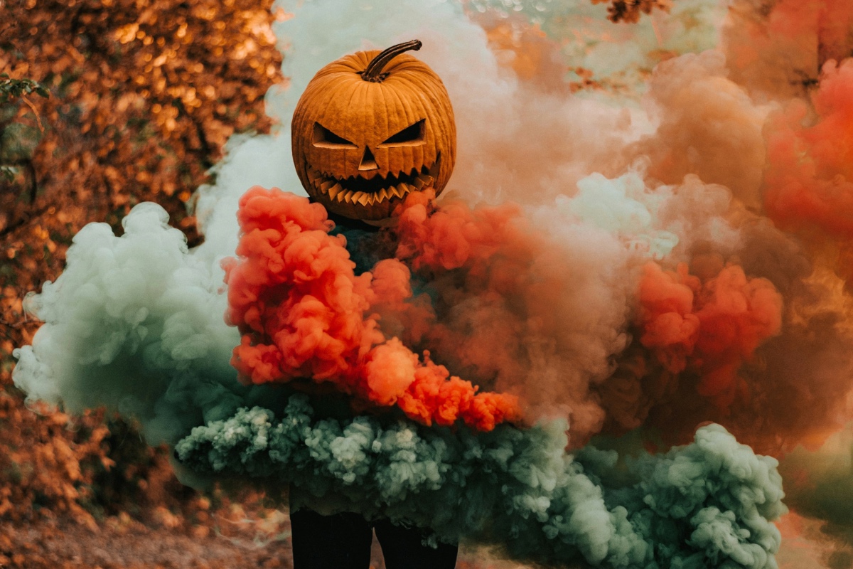 Person in a scary jack-o'-lantern costume surrounded by green and orange smoke, ideal for a spooky cannabis Halloween theme.