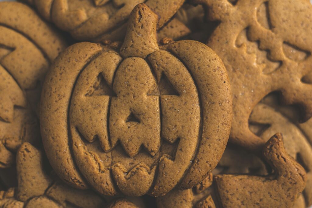 A large, central Halloween-themed gingerbread cookie shaped like a carved jack-o'-lantern, resting on a pile of other subtly shaped cookies.