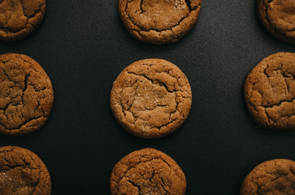 Overhead, close-up view of freshly baked, chewy ginger molasses cookies with cracked tops, arranged on a dark, matte black background.