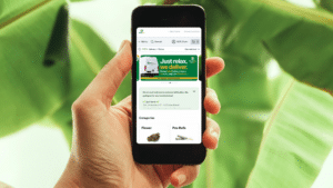 A person holding a smartphone displaying the NatureMed cannabis delivery app, showing the online menu for flower and pre-rolls with a banner promoting a 10-mile delivery radius in Gladstone.