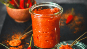 Homemade spicy red pepper condiment in a sealed jar, showing a thick texture for spreading on grilled burgers and summer sandwiches.