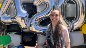 Voted Best Budtender AJ Gardner smiling in front of giant silver 420 balloons during a celebration at NatureMed cannabis dispensary in Gladstone.