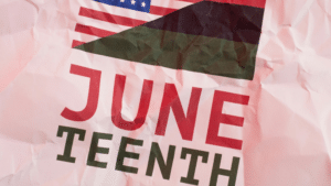 Close-up of a crumpled poster with large red 'JUNE' letters and dark text reading 'TEENTH' on a pink background, plus a flag graphic crossing the scene.